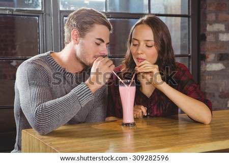 Smiling friends sharing smoothie and drinking through straws at coffee shop