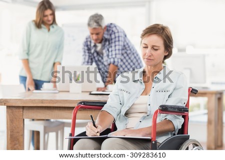 Casual businesswoman in wheelchair taking notes in the office