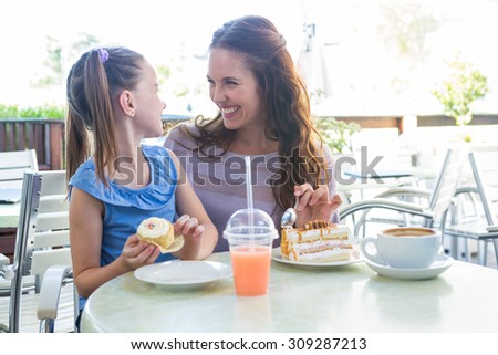 Mother and daughter enjoying cakes at cafe terrace on a sunny day