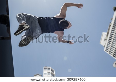 Athletic man doing back flip in the city on a sunny day
