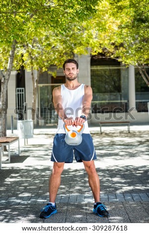 Portrait of a handsome athlete outfit with a kettlebell on a sunny day