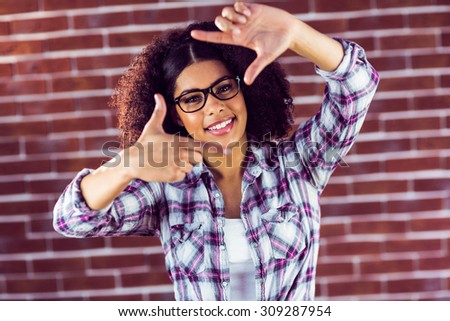 Portrait of attractive hipster taking picture with hands against red brick background