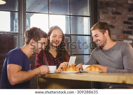 Smiling friends enjoying coffee and croissants together at coffee shop