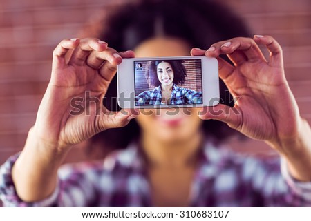 Attractive young woman taking selfies with smartphone against red brick background