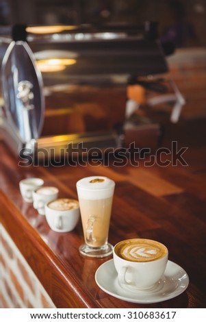 Several hot beverages in a row on the counter at coffee shop