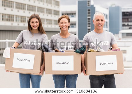 Portrait of smiling volunteers holding donation boxes on roof of building