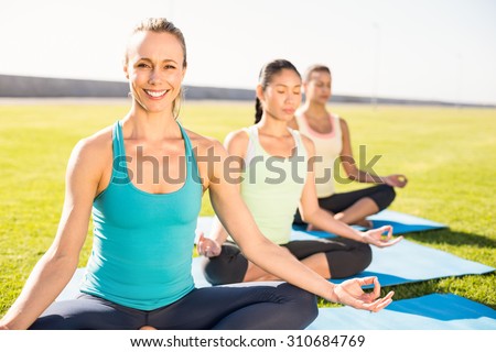 Portrait of smiling sporty blonde doing yoga with her friends in parkland