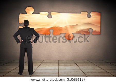 Businessman standing back to the camera with hands on hip against sun shining over mountains