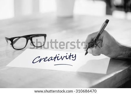 The word creativity against side view of hand writing on white page on working desk