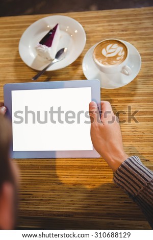 Man with tablet having cappuccino and cake at coffee shop