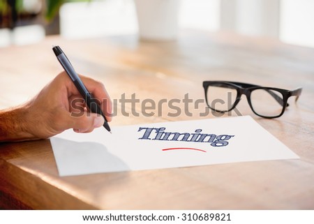 The word timing against side view of hand writing on white page on working desk