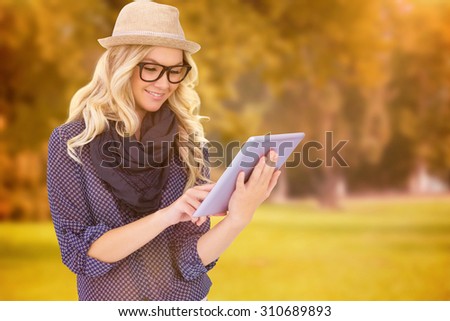 Smiling trendy blonde using tablet computer against trees and meadow