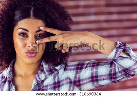 Portrait of attractive young woman showing peace sign against red brick background