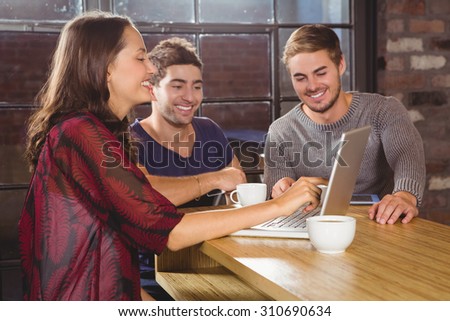 Smiling friends having coffee together and looking at laptop at coffee shop