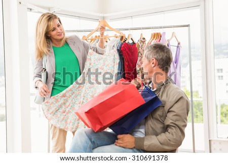 Woman showing dress to her sitting man in clothing store