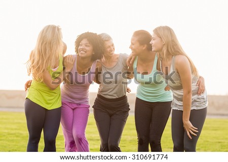 Smiling sporty women with arms around each other in parkland