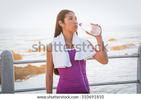 Fit woman resting and drinking water at promenade on a sunny day