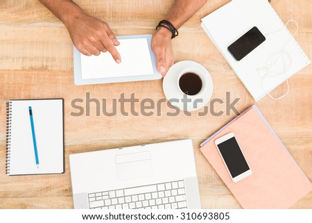 Hands using tablet next to several devices on wooden desk