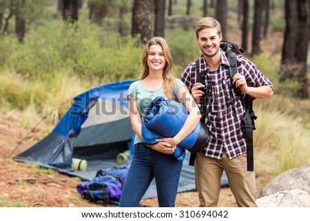 Portrait of a young pretty hiker couple holding a sleeping bag and backpack in the nature