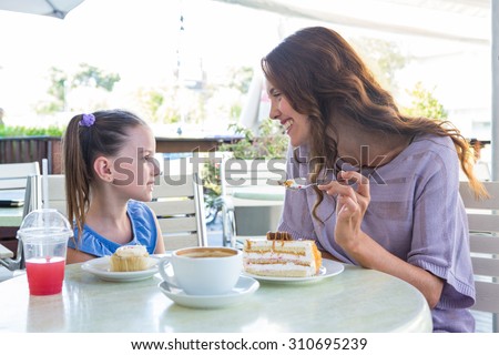 Mother and daughter enjoying cakes at cafe terrace on a sunny day