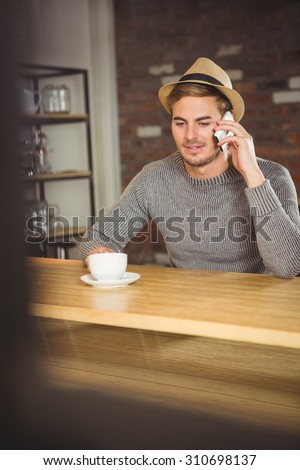 Handsome hipster having coffee and phoning at coffee shop