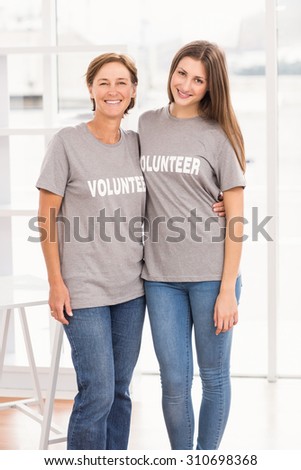 Portrait of smiling female volunteers putting arms around each other in the office
