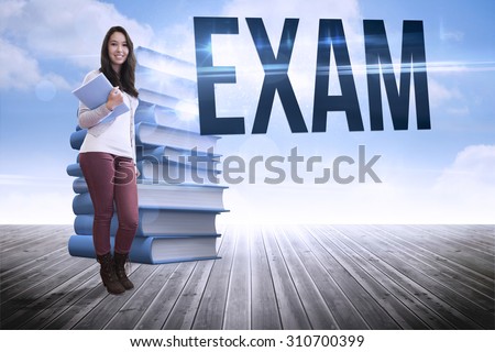 The word exam and smiling student holding textbook against stack of books against sky