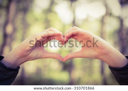 Carefree female hiker framing heart with hands in the nature