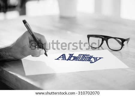 The word ability against side view of hand writing on white page on working desk