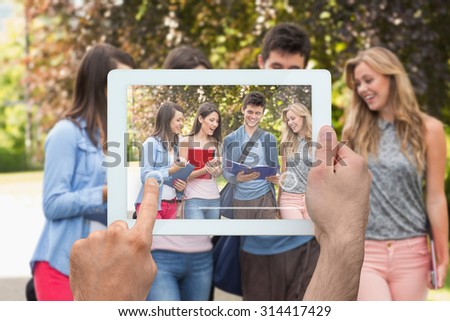 Hand holding tablet pc against happy students walking and chatting outside