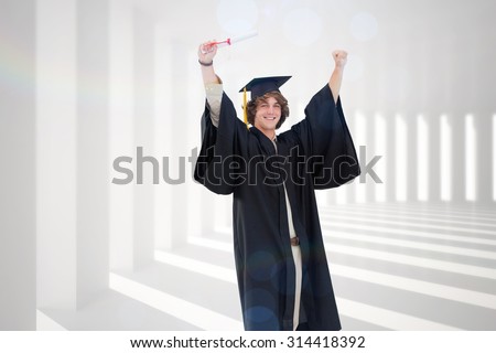 Male student in graduate robe raising his arms against curved white room