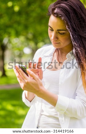 Beautiful brunette in the park sending text on a sunny day