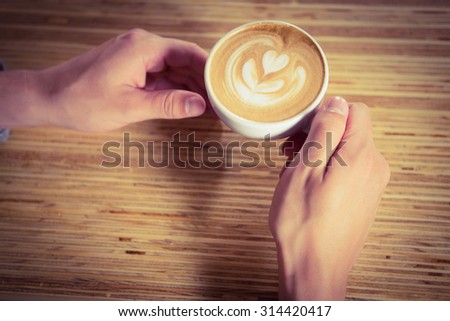 Hands holding cappuccino with coffee art at coffee shop