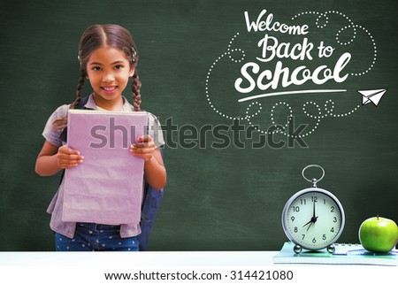Cute pupil smiling at camera holding notepad against green chalkboard