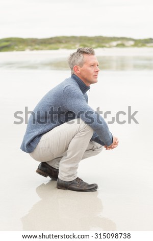 Man crouched down at the shore of the beach