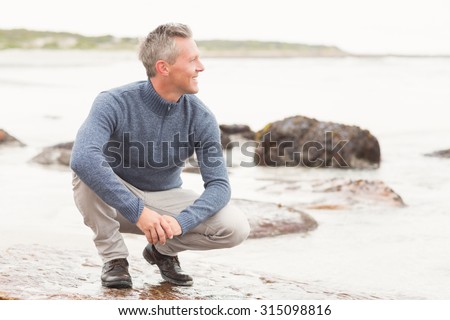 Man crouched down on a large rock by the shore