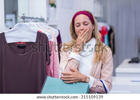 Tired woman with shopping bags yawning in clothing store