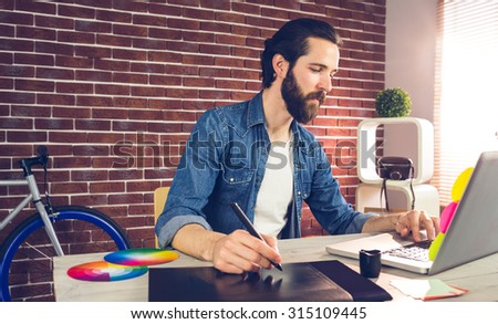 Businessman writing on graphic tablet while using laptop in creative office