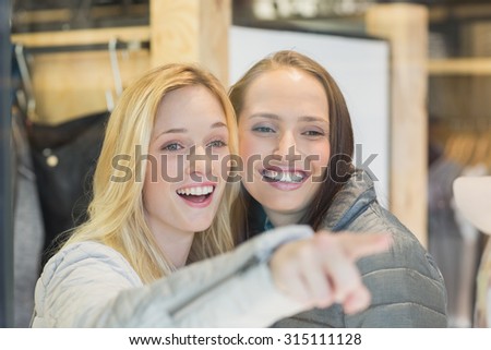 Two smiling female friends pointing away in clothes store