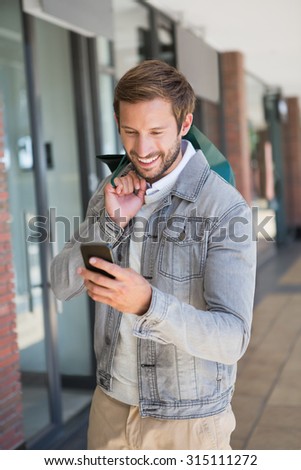 Young happy smiling man holding shopping bags and looking at his mobile in front of a store