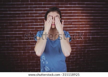 Pretty brunette with hands over eyes on red brick background
