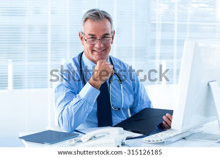 Portrait of smiling male doctor sitting at desk with file in hospital