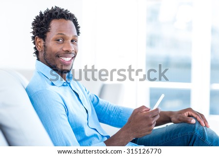 Portrait of smiling man holding mobile phone while sitting on sofa at home