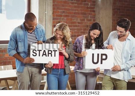 Portrait of smiling business people showing card with start up text while standing in bright creative office