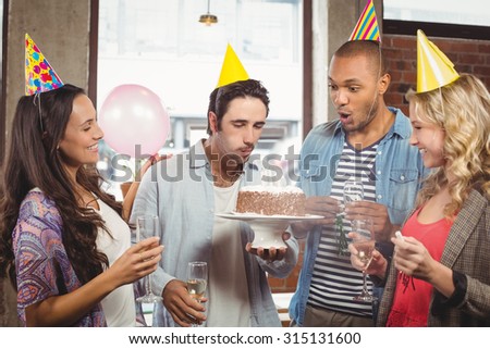 Man blowing candle on cake while colleagues smiling in office