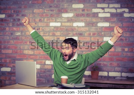 Happy businessman cheering while looking at laptop in office