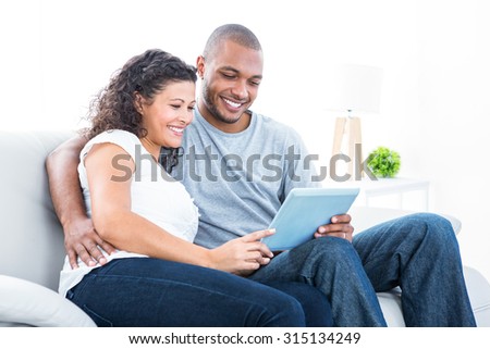 Young couple looking at tablet computer sitting on sofa in house