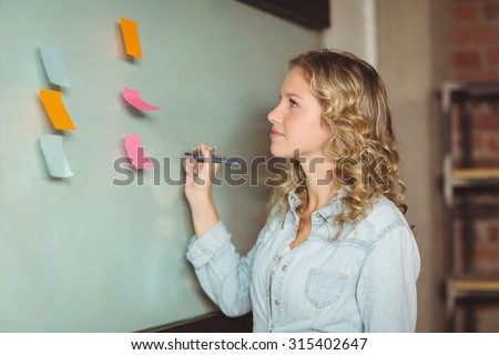Confident businesswoman holding marker while standing by glass board in creative office