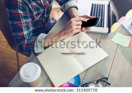 Midsection of creative editor using cellphone and laptop at office