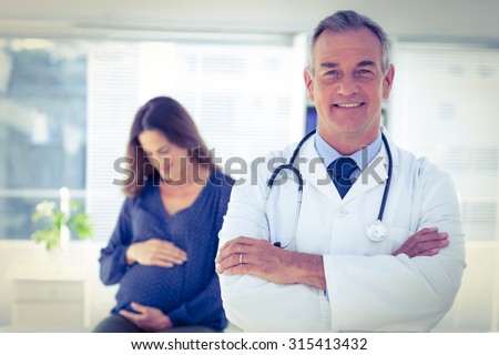 Portrait of confident male doctor with pregnant woman in background at clinic